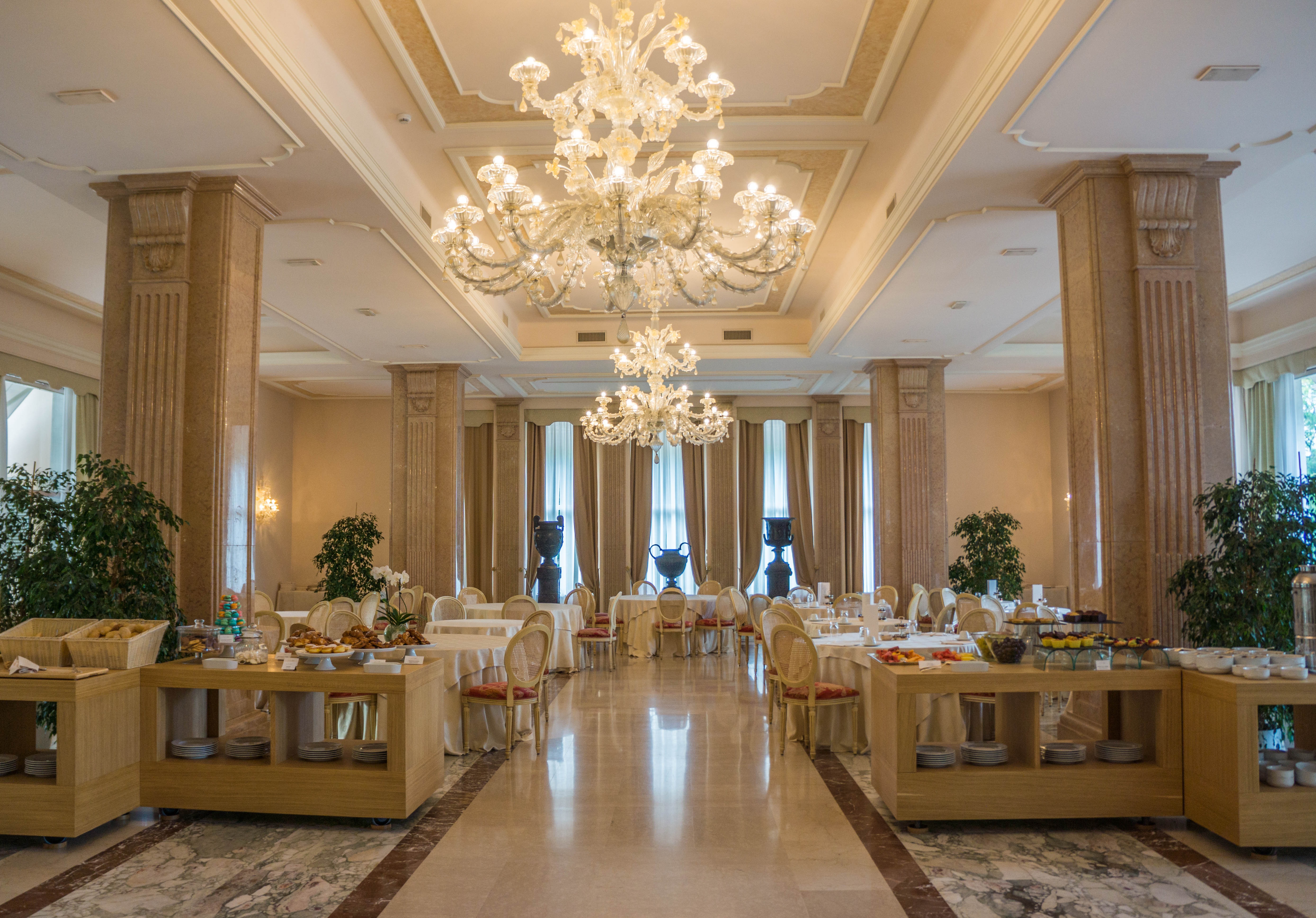 Grand hotel dining room with crystal chandeliers, marble columns, and elegant table settings.
