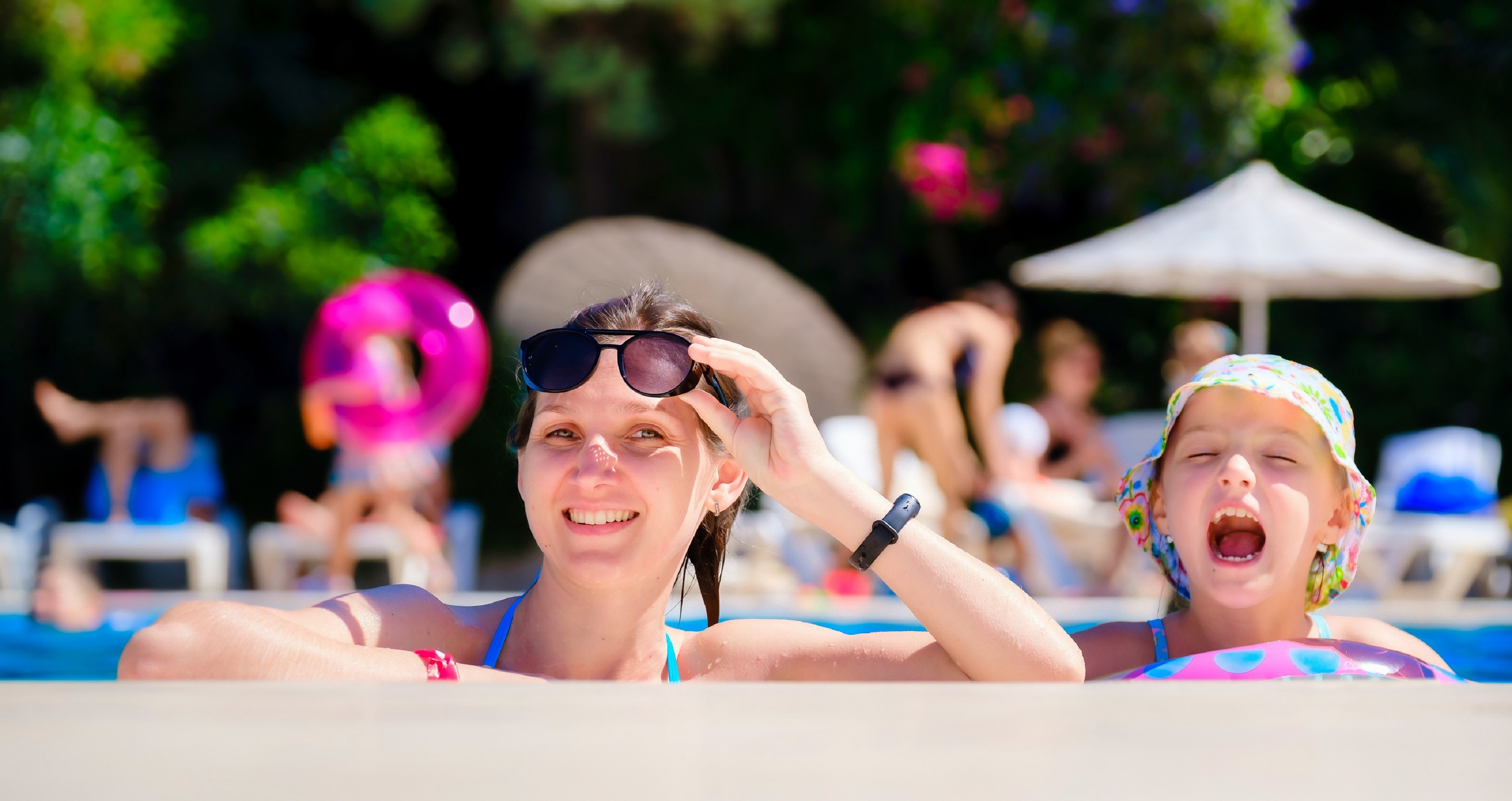 Mom and daughter laughing together in a hotel pool on a sunny day.